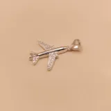 Dije con forma de avión plateado, con incrustaciones de circones brillantes en las alas y la cola. Posee un gancho para colgar en la parte superior.