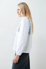 Remera blanca de estilo boho con bordados en el escote y mangas largas. Presenta escote en V con lazos y borlas. Corte recto y holgado.