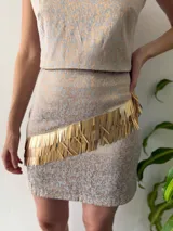 Falda corta de brocado color beige con estampado floral en gris claro y aplique de flecos dorados en diagonal.