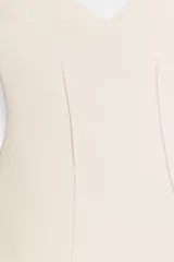 Top color crema o blanco roto, sin mangas, con escote corazón y corte ajustado al cuerpo con un ligero vuelo en el bajo.