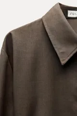 Camisa marrón de Zara Woman Collection, confeccionada en hilatura con viscosa. Tiene cuello solapa, manga larga con puño, bolsillo de plastrón en el pecho, cinturón ajustable con lazadas y bajo asimétrico. Se cierra con botones frontales.