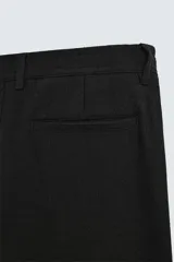 Pantalón negro de corte regular fit, con bolsillos laterales y bolsillos traseros de vivo. Presenta un bajo con vuelta y cierre frontal con cremallera y botón.