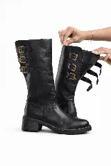 Bota biker de caña alta, color negro, confeccionada en cuero liso. Presenta tres correas ajustables con hebillas doradas en la caña y suela de goma gruesa con tacón bajo y ancho.