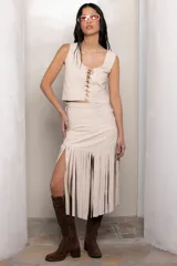Falda midi color beige confeccionada en cuero, con tajo lateral y flecos hasta media pierna. Presenta detalle de trenzado en los laterales.