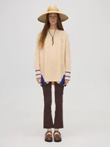 Sweater color crema con tejido en ochos, cuello redondo, puños acanalados con doble raya azul y tajos a los costados.