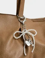 Cartera shopper negra de cuerina con manijas superiores y acceso mediante broche imantado. Incluye charm de perlas en forma de moño.