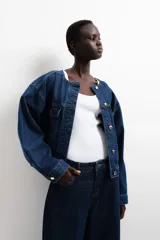 Campera de denim azul oscuro de algodón grueso con cuello redondo y solapa rompevientos guateada con botones ocultos. Modelo de corte holgado con hombros apenas caídos y puños ceñidos con botón. Bolsillos superiores con solapa y botón, bolsillos laterales discretos y trabillas ajustables con botón en el bajo.