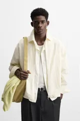 Sobrecamisa color crema de tejido técnico ligero, corte regular fit, cuello solapa, manga larga con puños abotonados, bajo ajustable con elástico en laterales y cierre frontal con cremallera.