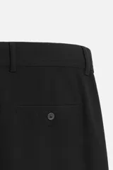 Pantalón slim fit negro confeccionado en tejido con elasticidad en ambas direcciones. Cuenta con bolsillos frontales y traseros de vivo con botón. Cierre frontal con cremallera y botón.