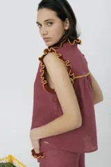 Blusa color borgoña con cuello alto y mangas cortas, con detalle de volados tejidos en color mostaza en cuello, mangas y bolsillos.