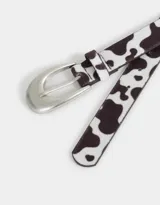 Cinturón de cuero sintético con estampado de vaca y hebilla metálica plateada.