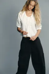 Camisa blanca de cuello bobo con bordados, escote pico con lazada, manga corta abullonada con elástico y cierre frontal con botones.