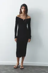Vestido largo de punto negro con escote recto, hombros descubiertos, mangas largas y detalle de pieza metálica en el delantero.