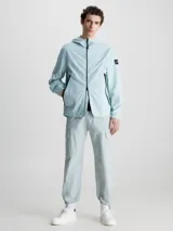Campera con capucha Calvin Klein, confeccionada en nailon 100% reciclado color celeste. Tiene cierre de cremallera frontal, cuello alto, bolsillos delanteros con cremallera, puños y dobladillo elásticos, tirador de cremallera con la marca e insignia con el logo de Calvin Klein en la manga.
