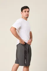 Bermuda deportiva de nylon color verde militar, de corte suelto, con cintura elástica, cordón de ajuste, detalles de líneas en los costados y bolsillos con cierre.