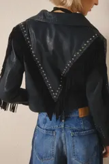 Campera corta de cuero color negro, con flecos en espalda y mangas, tachas metálicas y símil piedra cristal. Cierra con broches en el frente, tiene forrería y bolsillo interno.
