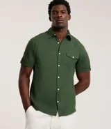 Camisa de hombre de manga corta en lino color blanco, con cuello clásico, botonadura frontal y bolsillo de parche en el pecho. Corte recto.