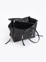 Bolso tote pequeño de cuero vacuno negro, con cierres funcionales en los laterales para mayor apertura y espacio. Incluye bolsillo cruzado interno y tag con aplique metálico.