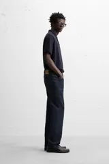 Jeans de corte slim fit confeccionados en denim de algodón sin lavados, color azul oscuro. Cierre frontal con botones y cinco bolsillos.