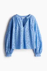 Blusa celeste con bordado calado, de corte holgado, cuello mao con frunces, abertura en V adelante y mangas globo largas de corte raglán con puños abotonados.