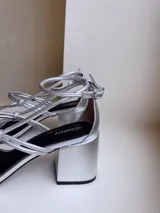 Sandalias negras de cuero con tiras finas con nudos en el empeine y pulsera con hebilla en el tobillo. Tacón bloque de 7cm.