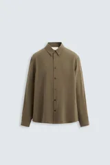 Camisa negra de corte relaxed fit confeccionada en tejido fluido con mezcla de viscosa. Tiene cuello solapa, manga larga con puño abotonado y cierre frontal con botones.