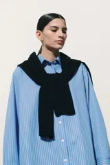 Camisa celeste y blanca a rayas verticales, de corte amplio y mangas largas con puños abotonados. Cuello clásico y cierre frontal con botones.