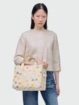 Bolso tote mediano de lona color crema con estampado de margaritas de colores, doble asa corta y correa larga extraíble.