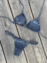 Conjunto de bikini azul con efecto desgastado, compuesto por un corpiño de triángulos movibles con tiras finas para atar al cuello y a la espalda, y una bombacha vedetina con tiras regulables con hebilla a los costados.