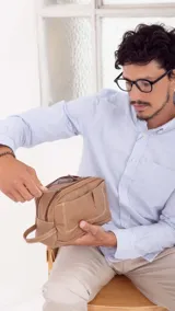 Neceser marrón oscuro de símil cuero con dos divisiones independientes con cierre superior individual. Ambas divisiones cuentan con bolsillos internos. Tiene un bolsillo al frente con broche magnético, bolsillo con cierre atrás y asa de mano lateral.