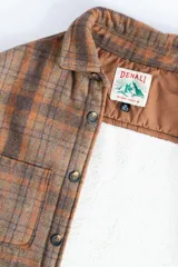 Camisa leñadora a cuadros marrón y naranja, forrada en corderito sintético, con cuello clásico, cierre frontal con botones, dos bolsillos frontales con tapa y puños abotonados.