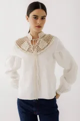 Blusa beige de lino con cuello alto y pechera de crochet. Mangas largas abullonadas con puños elásticos.