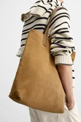 Bolso tipo shopper color marrón claro, fabricado en cuero con acabado serraje. Tiene doble asa de mano de cuero y un bolsillo interior con cierre.