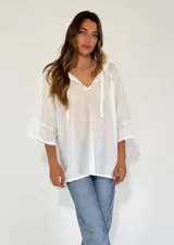 Blusa blanca de mangas 3/4 con volados y escote en V con cordones.