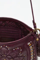 Cartera de cuero negro con diseño de flor mandala en relieve y apliques de tachas doradas y plateadas. Presenta flecos colgantes en uno de los laterales y correa ajustable para llevar al hombro o cruzada.