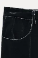 Pantalón de terciopelo negro de tiro medio, con bolsillos delanteros y traseros, pierna recta y cierre frontal con cremallera, botón y gancho metálico.