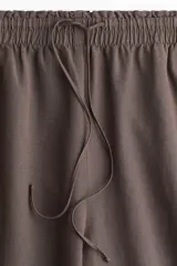 Pantalón marrón de lino, corte holgado, tiro alto, cintura elastizada con cordón ajustable, bolsillos laterales y pierna ancha.