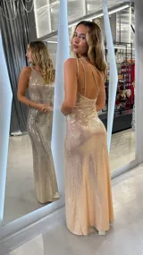 Vestido largo dorado con lentejuelas, escote asimétrico y espalda descubierta con tiras cruzadas. Corte ajustado al cuerpo.