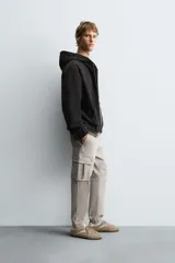 Pantalón cargo negro de corte slim fit, confeccionado en tejido de algodón con cintura elástica ajustable con cordón. Cuenta con bolsillos frontales, traseros y bolsillos tipo parche con solapa en los laterales.