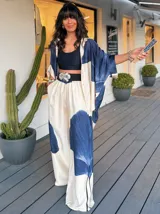 Pantalón palazzo de satén color crema con estampado de flores abstractas en azul y rayas verticales finas en negro. Cintura alta con cinturón ancho negro con hebilla plateada en forma de flor.