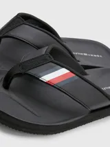Ojotas negras Tommy Hilfiger con tira ancha de poliuretano acolchada y suela de goma EVA. Detalle de cinta distintiva con los colores de la marca en la tira.