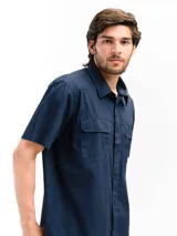 Camisa de manga corta color beige con cuello clásico, cierre frontal con botones, dos bolsillos con solapa abotonada en el pecho y corte recto. Ideal para actividades al aire libre.