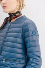 Campera azul de nylon con relleno de pluma, corte holgado a la cintura, cuello redondo y cierre frontal. Tiene bolsillos con cierre y detalle de vivos.