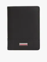Billetera plegable de cuero negro con tres ranuras interiores para tarjetas y dos compartimentos interiores para billetes. Incluye cinta distintiva en el interior y logo alargado de Tommy Hilfiger esmaltado en la parte delantera.