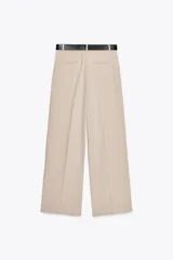 Pantalón negro de tiro alto con pinzas delanteras, pernera ancha y cinturón con hebilla dorada.