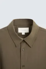 Camisa negra de corte relaxed fit confeccionada en tejido fluido con mezcla de viscosa. Tiene cuello solapa, manga larga con puño abotonado y cierre frontal con botones.