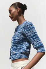 Chaqueta de punto azul y blanco con cuello redondo y manga francesa. Tiene bolsillos delanteros de plastrón y cierre frontal con botones a tono.