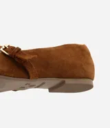Zapatilla chatita femenina en gamuza color marrón, con punta redonda y tira con hebilla lateral.