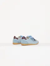 Zapatilla de cuero marrón con detalles en verde y suela de goma. Tiene cordones rosas y un dije colgante con forma de abeja.