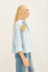 Camisa celeste de poplin con bordados de palmeras doradas en el frente, de corte amplio, con cuello y cartera.